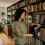 Femme rangeant un vinyle dans une bibliothèque murale combinant livres et disques dans un salon cosy