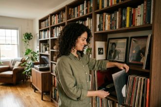 Femme rangeant un vinyle dans une bibliothèque murale combinant livres et disques dans un salon cosy