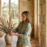 Femme arrangeant des plantes séchées dans un intérieur en pierre de Bordeaux pour transformer l'ambiance de sa maison en Gironde