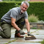 Homme effectuant l'entretien manuel d'une terrasse en pierre avec une brosse, nettoyage des joints de dallage extérieur