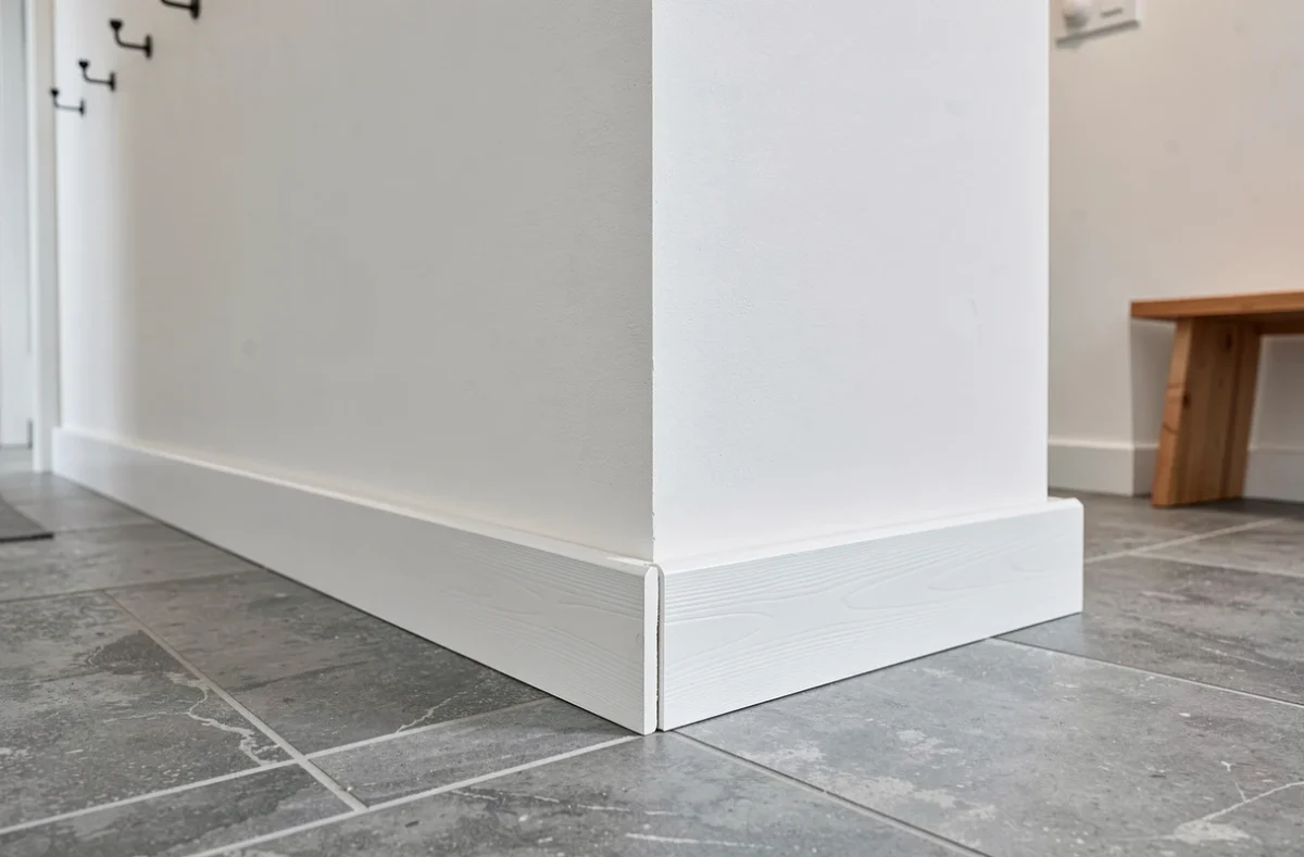 Angle intérieur de couloir avec cache plinthe bois peint en blanc révélant une erreur de pose courante