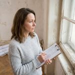 Femme tenant un devis budgétaire devant une vieille fenêtre en bois à rénover dans un salon