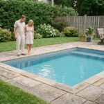 Couple examinant une piscine coque installée dans un jardin résidentiel avec terrasse en pierre naturelle