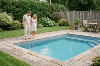 Couple examinant une piscine coque installée dans un jardin résidentiel avec terrasse en pierre naturelle