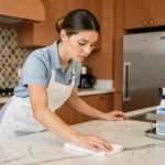 Femme de ménage professionnelle en uniforme bleu nettoyant un plan de travail en marbre dans un appartement moderne de Casablanca