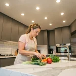 Cuisine moderne avec spots encastrables au plafond éclairant un plan de travail en marbre blanc, femme préparant des légumes frais